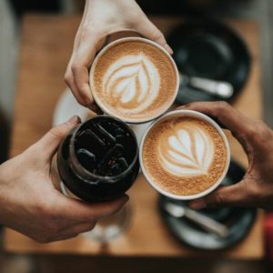 Overhead view of three cups of coffee being held by three hands.
