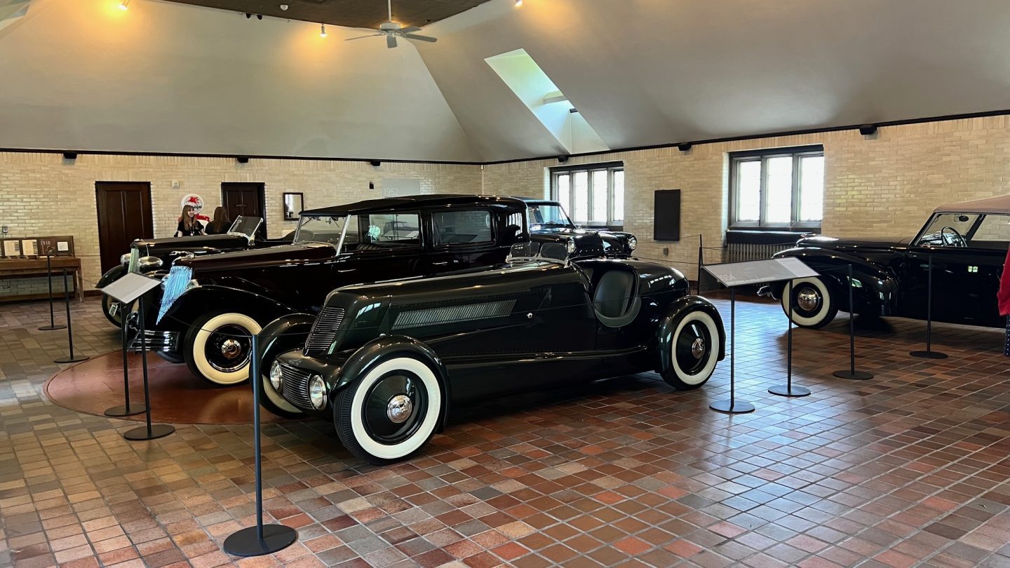 Close-up view of vintage Ford cars in a well-lit exhibit space with cream brick walls and large windows, emphasizing classic design and chrome details.
