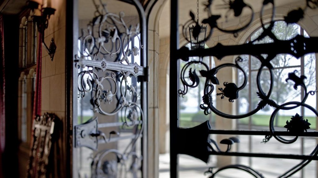 Wrought-iron doors by Philadelphia metalsmith Samuel Yellin open from the Ford House Main Hall to the loggia, featuring intricate Gothic-inspired scrollwork with views of Lake St. Clair beyond.