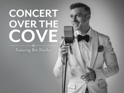 Promotional image of jazz vocalist Ben Sharkey wearing a white tuxedo and bow tie, singing into a vintage microphone on a grayscale background. Text reads: “Concert Over the Cove Featuring Ben Sharkey.”