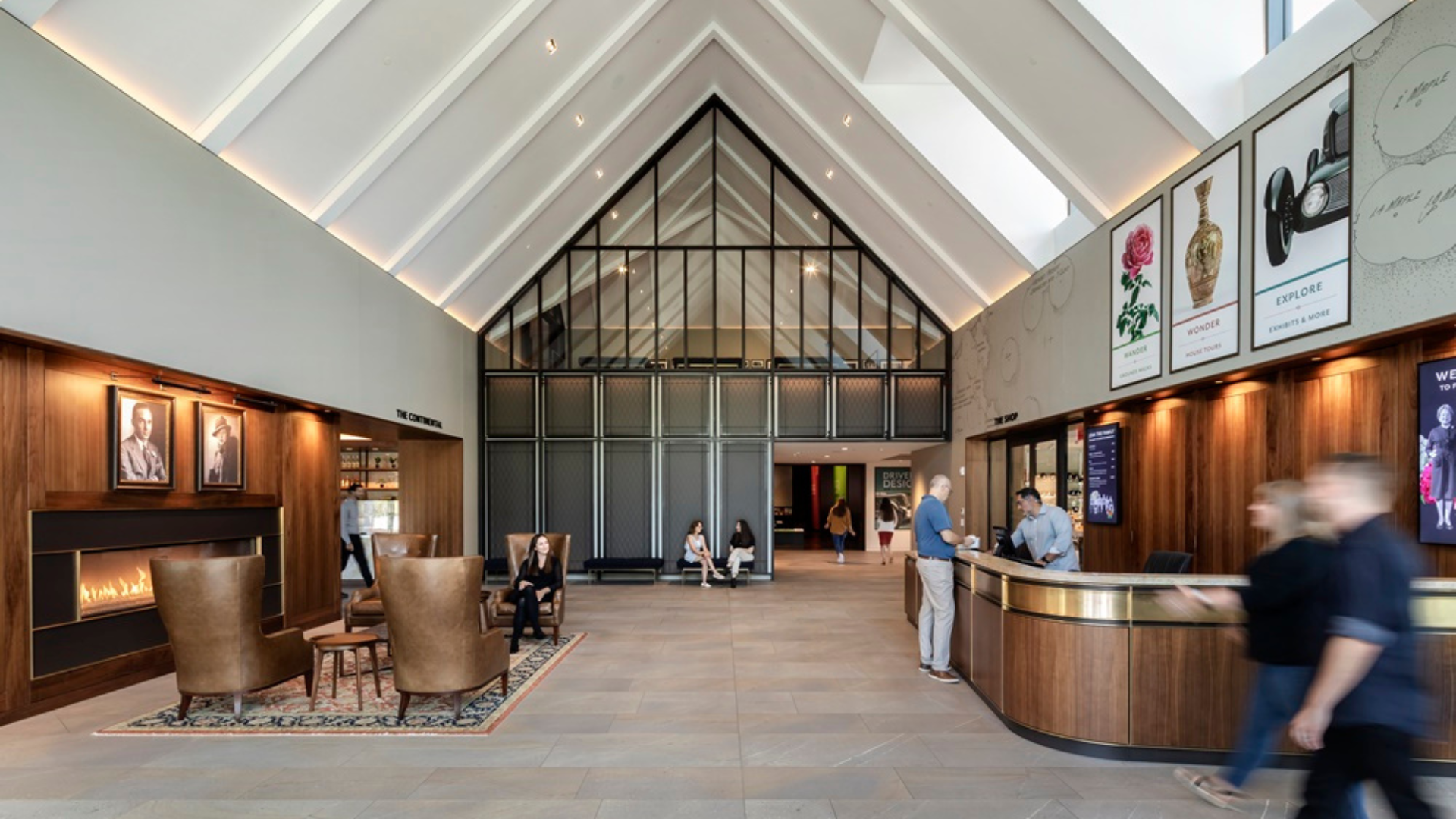Guests and staff inside the vaulted main lobby of Ford House’s Visitor Center, featuring the admissions desk, seating area, and fireplace.