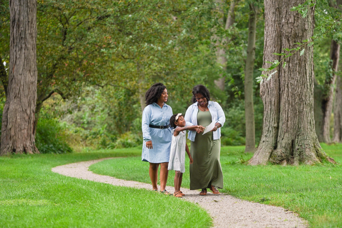 A grandmother, mother, and daughter enjoy a cheerful walk on a wooded path at Ford House.