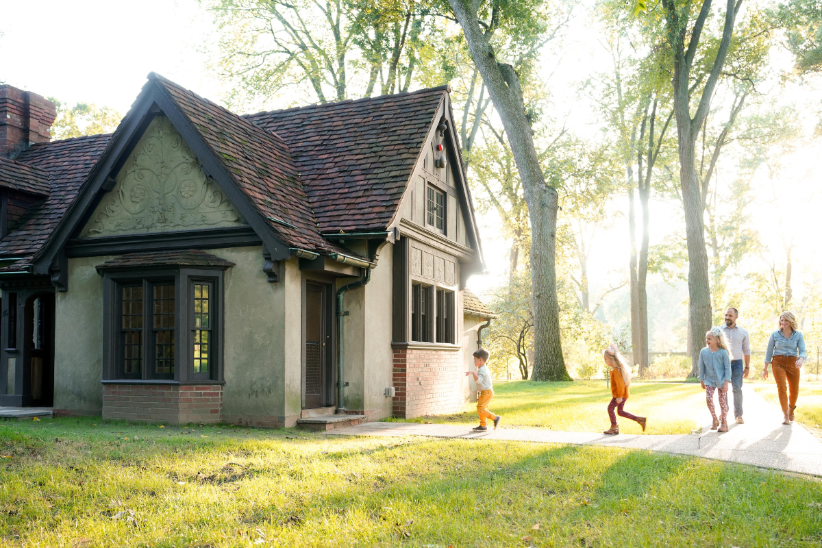 A family of five walks together near the playhouse at Ford House, bathed in soft evening sunlight.