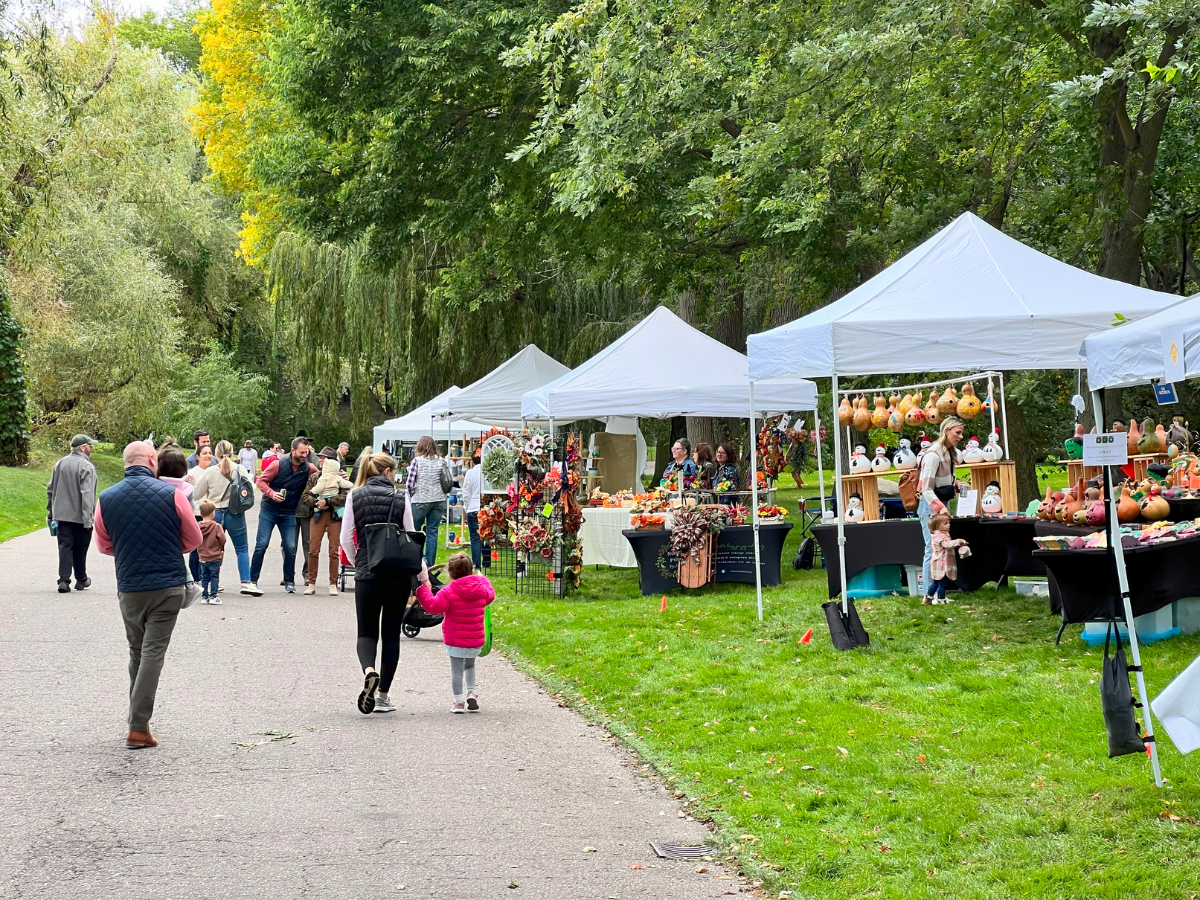 Pathway lined with vendor tents selling fall crafts and decorations at Harvest Day, with families walking and shopping.