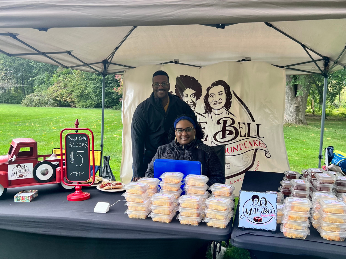 Vendor booth at Harvest Day featuring Mae Bell Pound Cakes, with two smiling sellers behind a display of packaged cake slices.