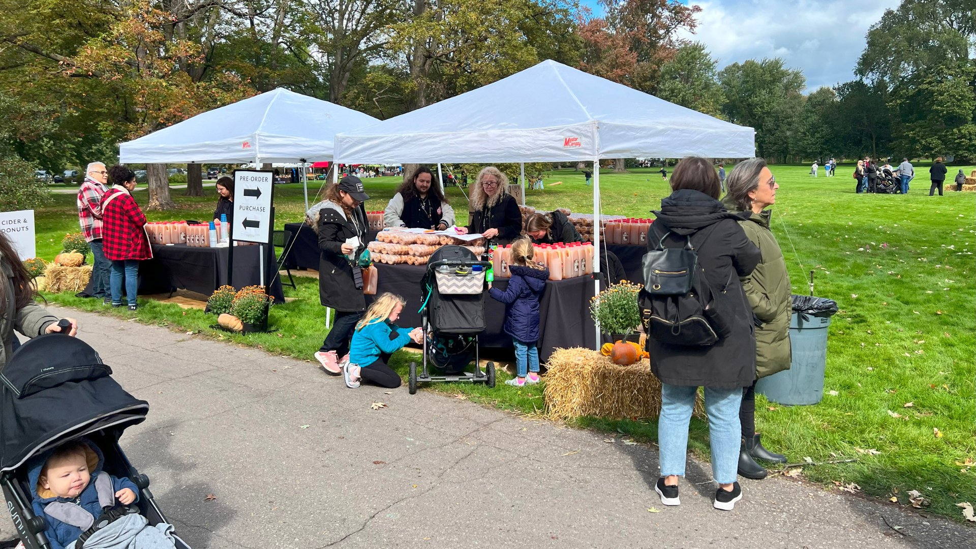 Families and children gather at a cider and donut booth with white tents, pumpkins, and hay bales, enjoying classic fall treats at Ford House’s Harvest Day.