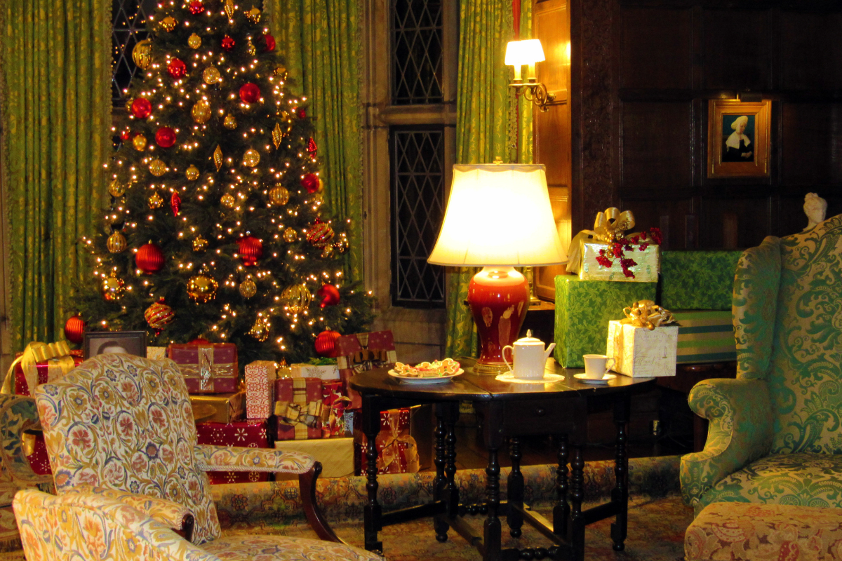 Cozy living room at Ford House decorated with a Christmas tree in gold and red ornaments, wrapped presents, and a tea service on a side table.