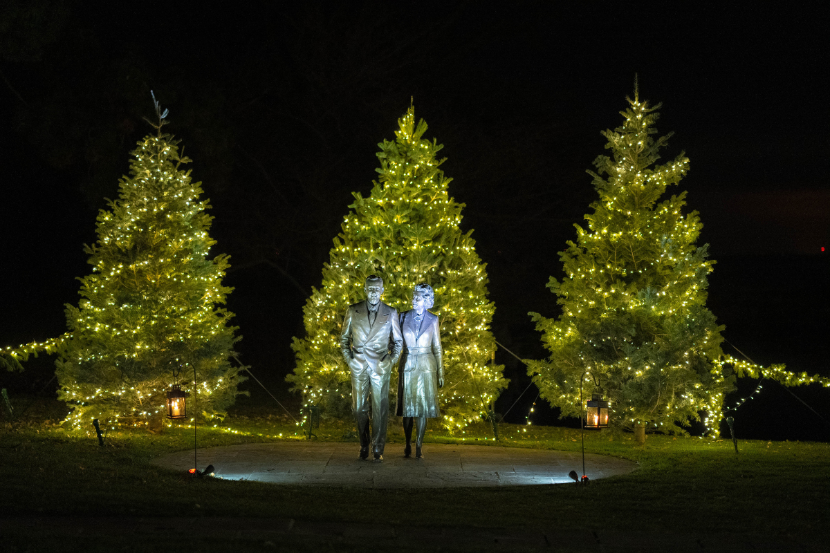 Bronze statues of Eleanor and Edsel Ford framed by three lit Christmas trees during Home for the Holidays at Ford House.