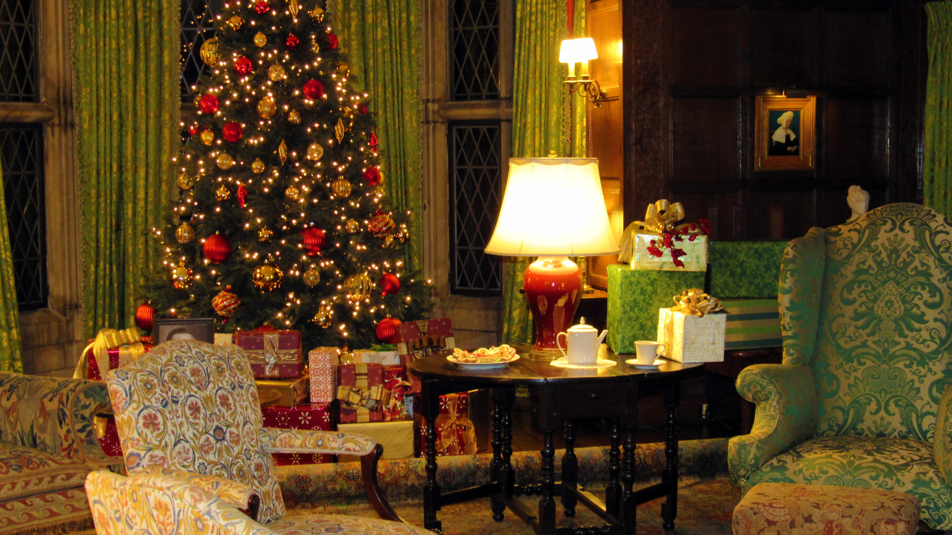 A warmly lit room at Ford House decorated for Home for the Holidays at Ford House, featuring a Christmas tree, wrapped presents, and vintage furniture.