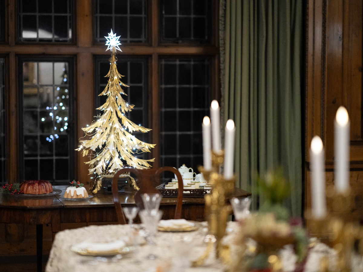 The Ford House dining room set for the holidays, featuring gold candlesticks, lace table linens, and a Christmas tree.