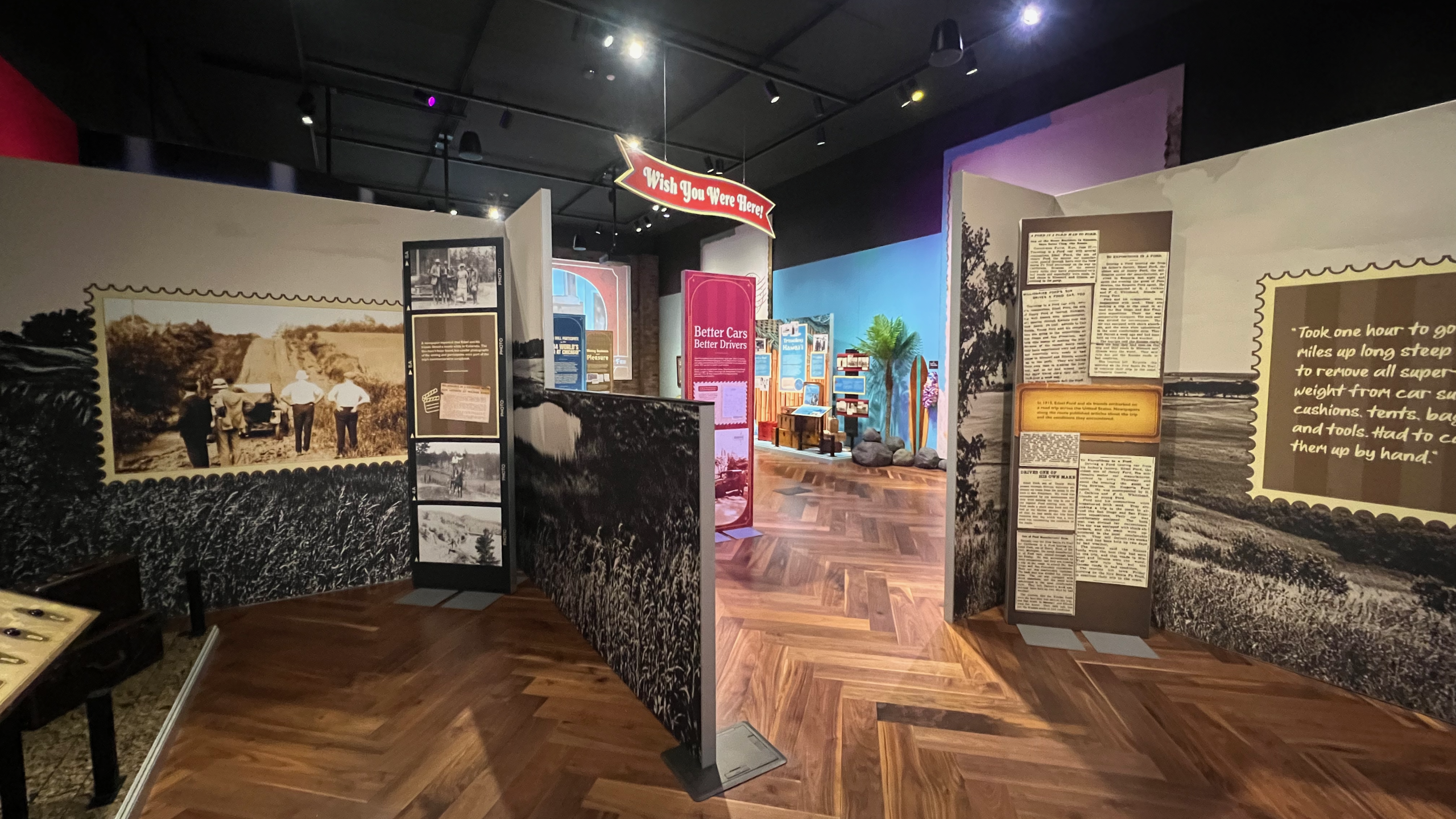 Exhibit section featuring a map of the United States with a red route line marking the 1915 trip path. The wall includes vintage newspaper clippings and a quote about removing car weight to climb steep hills, alongside photos of early automobiles and rough terrain.