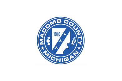 Official seal of Macomb County, Michigan in blue and white, with the county outline, gears, waves, a sailboat, and “1818” marking its founding year.