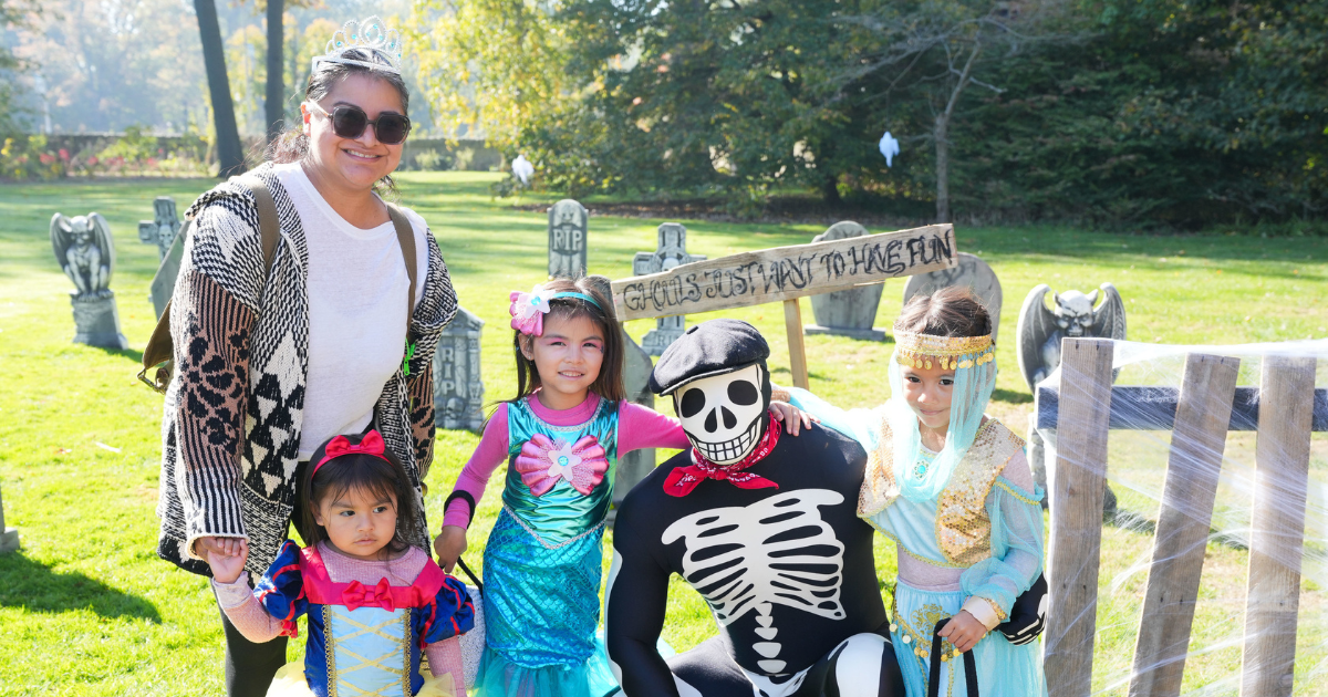 Families take a photo with a skeleton character among Halloween props at Ford House’s Little Goblins.