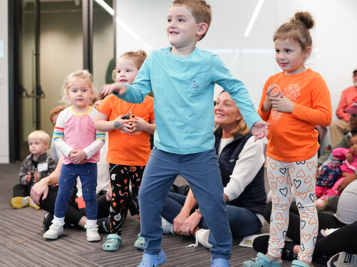 Group of preschool children dancing and laughing during an indoor Story Festival program.