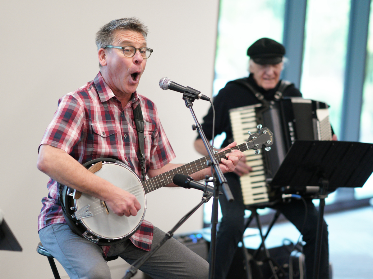 Jim Gill, Musician playing banjo and singing while another plays accordion at Story Festival.