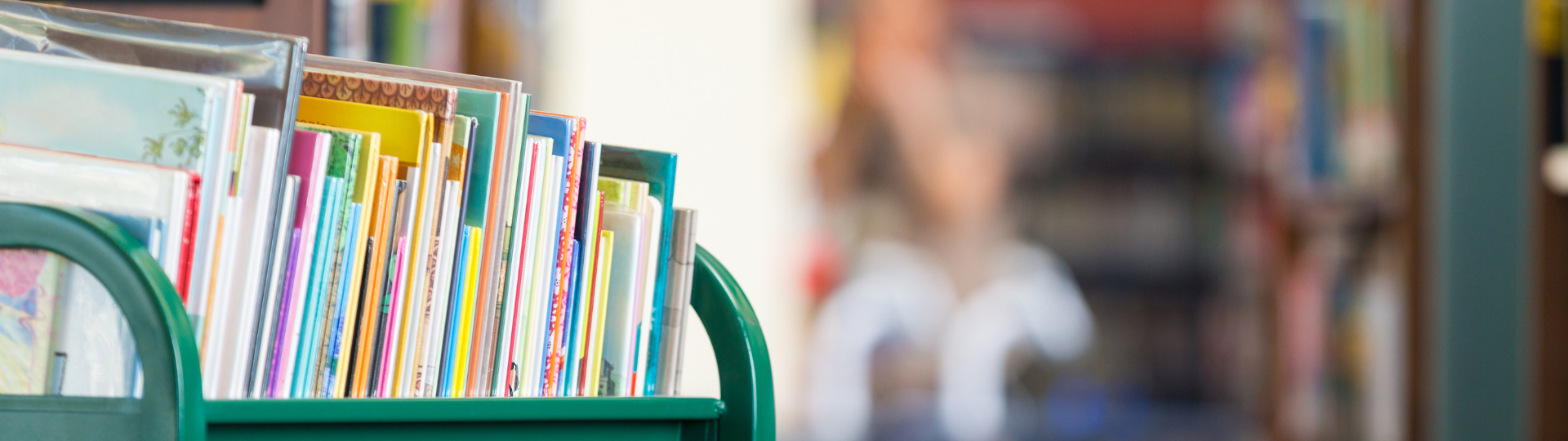 Row of colorful children’s books neatly arranged on a green library cart with a softly blurred background.